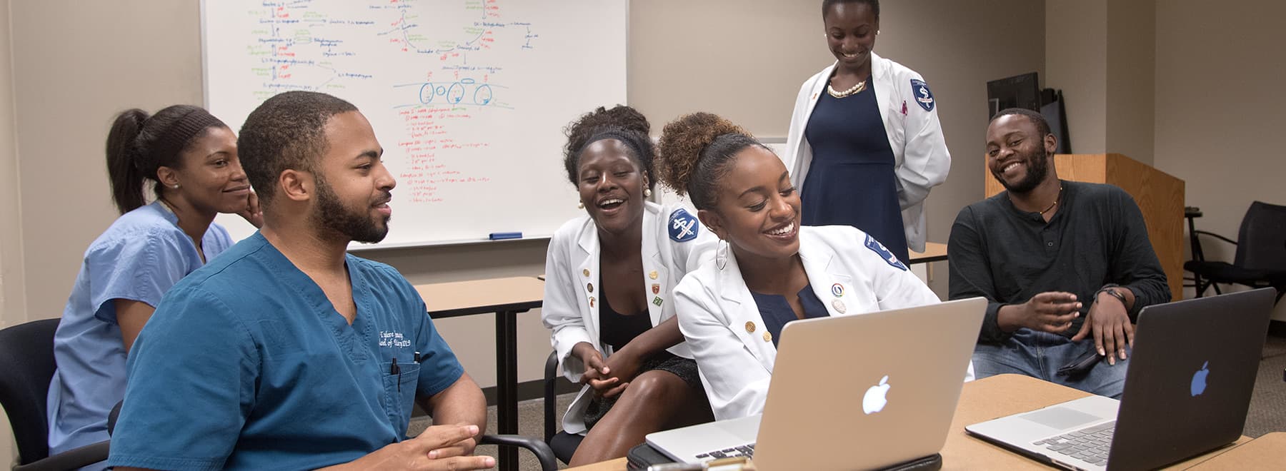 Group of male and female students gather around a laptop to work on a project.